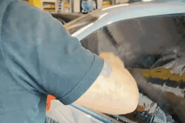 A technician carefully applies a window tint film to a car's side window, smoothing it out with precision to ensure a clean, bubble-free finish. The reflective film darkens the glass, indicating the installation of high-performance tinting.