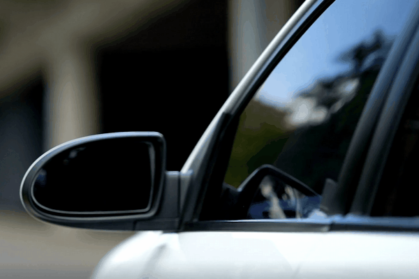 A close-up of a car window rolling up to reveal a dark privacy tint that allows clear visibility from the inside but obscures the view from outside. The reflective tint gives a sleek, modern look while enhancing interior privacy.