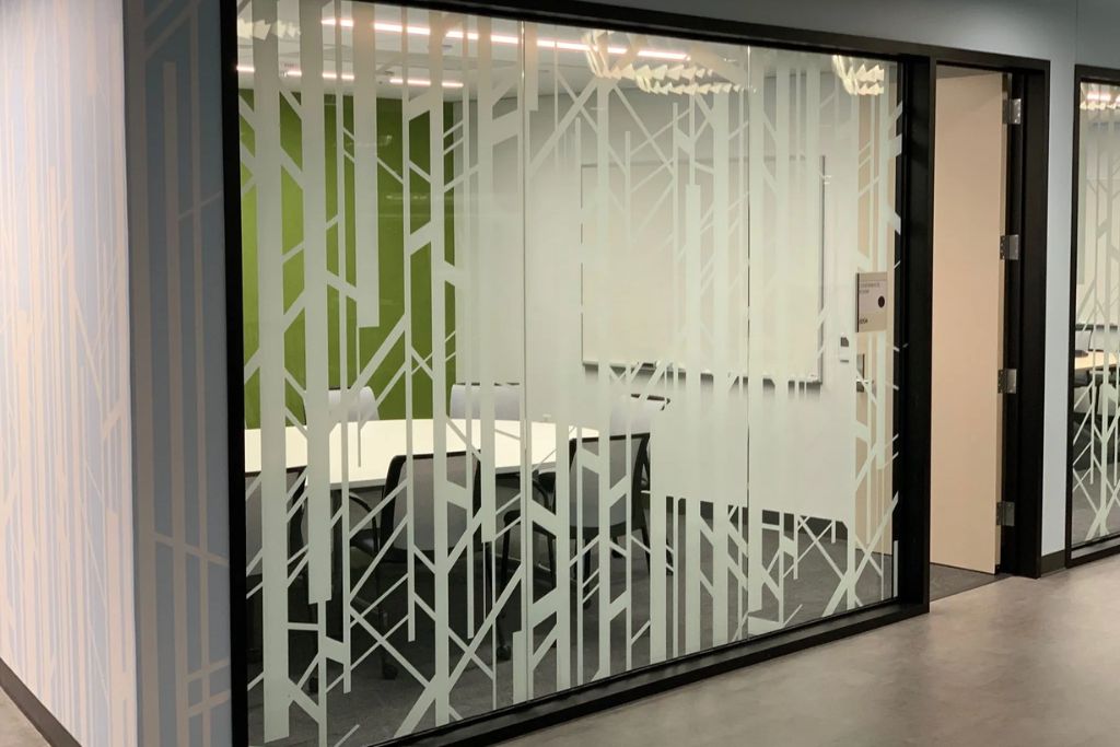 Glass walls of a modern office space are covered with a decorative privacy film featuring a geometric frosted pattern, allowing light through while obscuring the view into the meeting room.