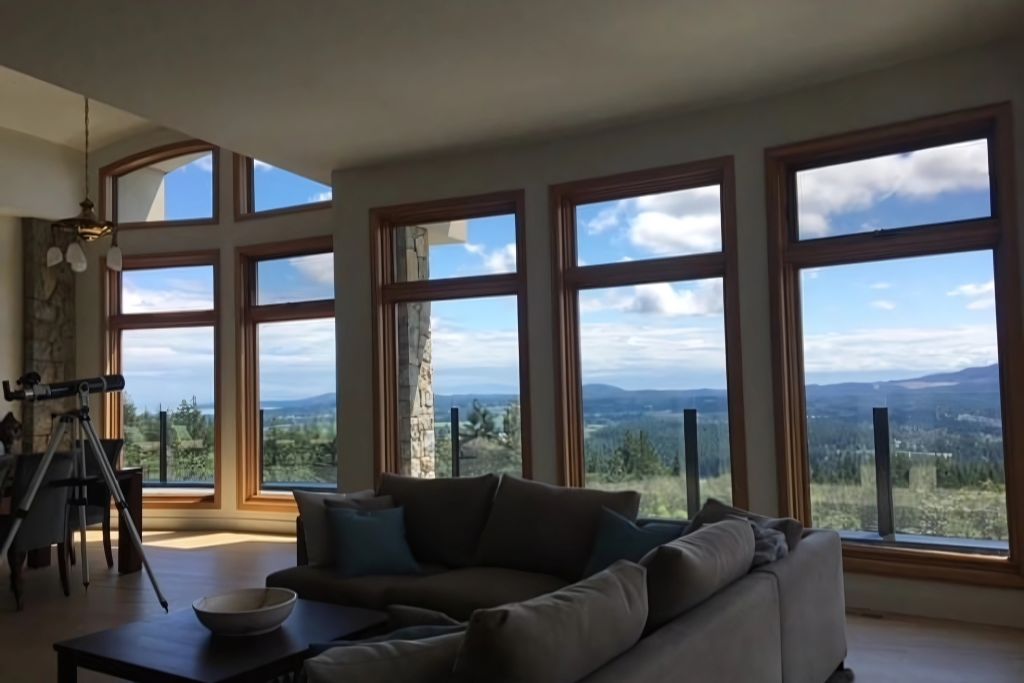 Spacious living room with large, clear windows offering a scenic mountain view. Despite the sunlit exterior, the room remains cool and comfortable, suggesting the windows are treated with virtually invisible Low-E insulating film.
