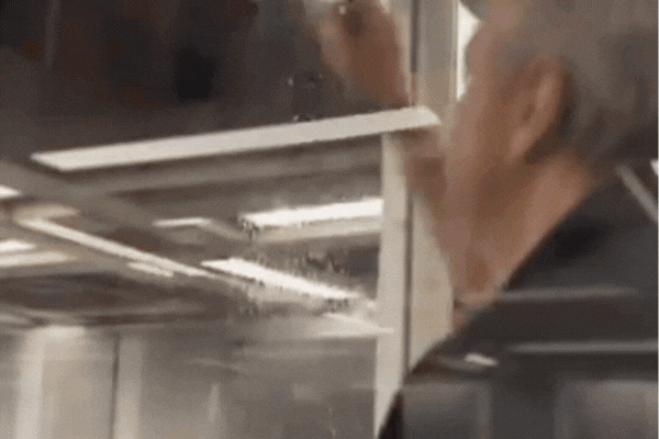 A person carefully applies window film to the inside of a glass pane, smoothing it out with a squeegee to eliminate air bubbles. The reflective surface of the film subtly darkens the window as it's installed.