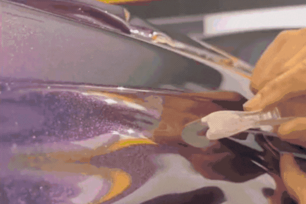 Close-up animation of a technician carefully applying a shimmering purple vinyl wrap to a car panel using a squeegee tool, smoothing out air bubbles and aligning the material precisely.