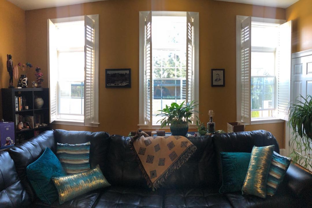 Sunlit living room in a historic Massachusetts home with plantation shutters and large windows treated with insulating window film, demonstrating home window tinting benefits without altering the home's classic character.
