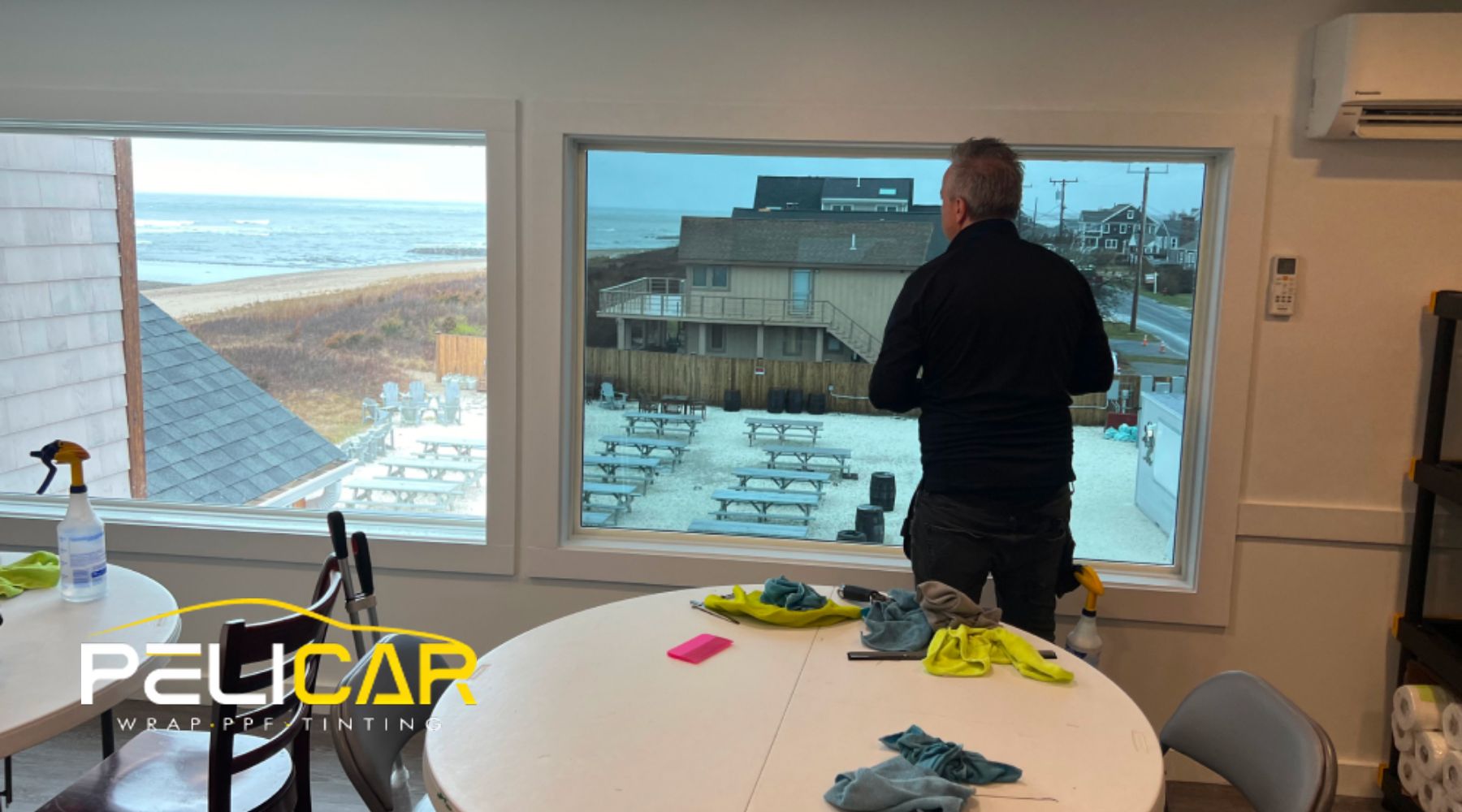 A Pelicar technician installs energy-efficient window tint in a coastal Massachusetts home, showcasing home window tinting benefits like reduced heat gain and improved insulation for year-round comfort.