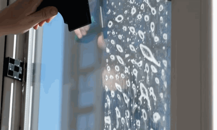 Technician applies commercial window tint film to the exterior of a large glass storefront, using tools and a spray solution for smooth installation.