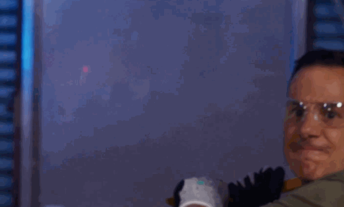 A man wearing safety goggles swings a blunt object toward a glass window during a security window film impact test, with no visible shattering.