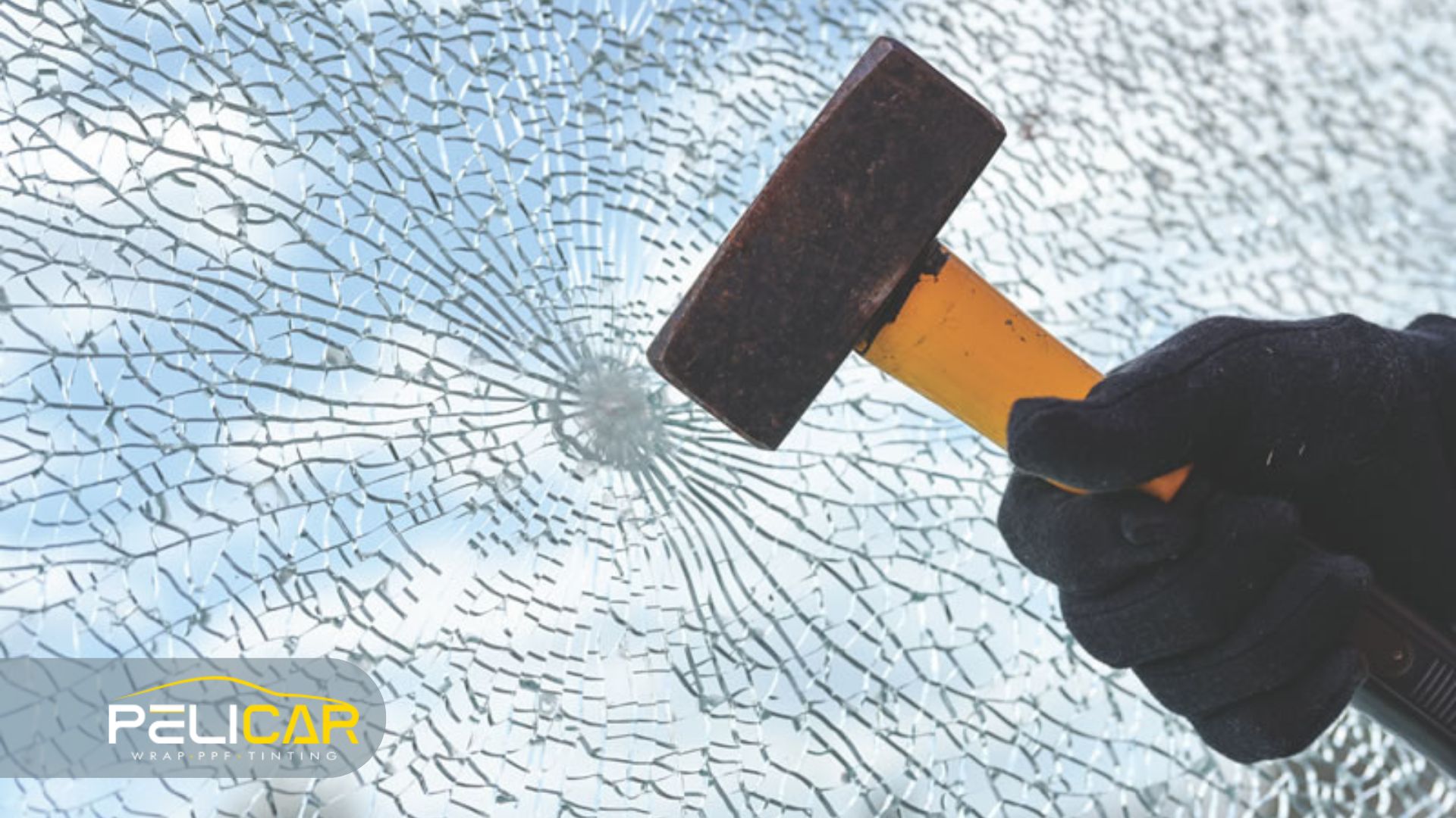 Close up of a gloved hand striking glass with a hammer creating a spiderweb crack pattern to demonstrate how Security Window Film helps businesses prevent glass from shattering and falling apart during forced entry attempts.