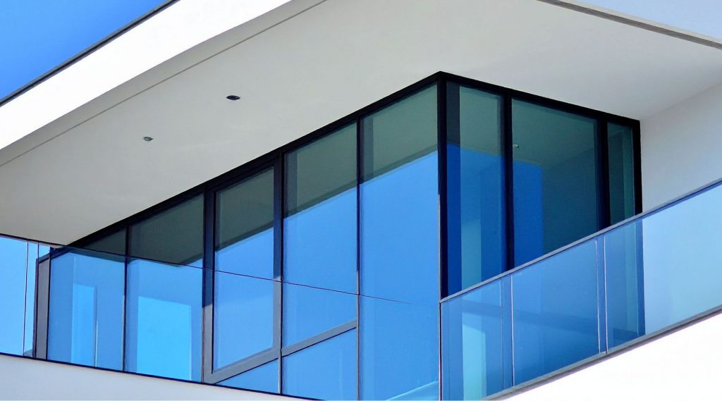 Modern commercial storefront with large floor to ceiling glass windows and blue tinted balcony panels illustrating the clean appearance preserved with security window film. The reinforced glass maintains transparency and natural light while adding discreet protection for retail spaces.