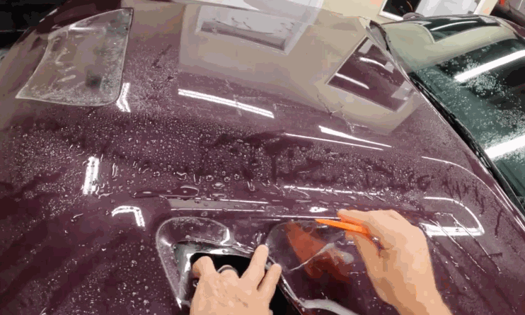 Installer carefully applies paint protection film around a car door handle using a tool while the surface is wet with solution. The process shows detailed work needed for seamless paint protection film coverage on complex areas.
