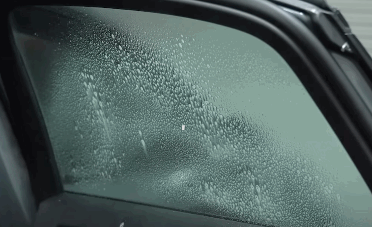 Car window covered in fine water droplets during the window tint prep process, showing moisture evenly spread across the glass before film application. The surface appears foggy as part of ensuring a clean and smooth tint result.