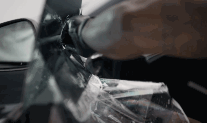 Close up of a car side mirror and door panel as a technician applies window tint film smoothly across the surface. The glossy black exterior reflects light while the film is carefully pressed into place to remove air bubbles.