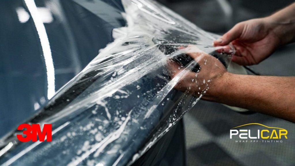 Paint protection film installation being carefully applied to a dark vehicle panel inside a professional auto shop.