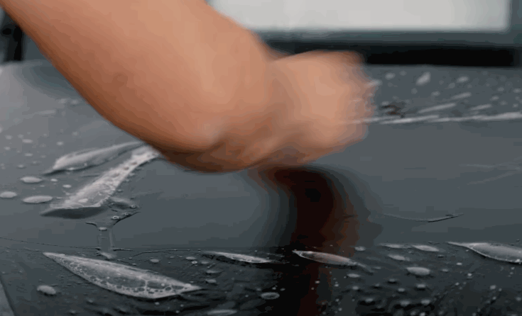Close-up of paint protection film application process on a black vehicle with installation solution visible.