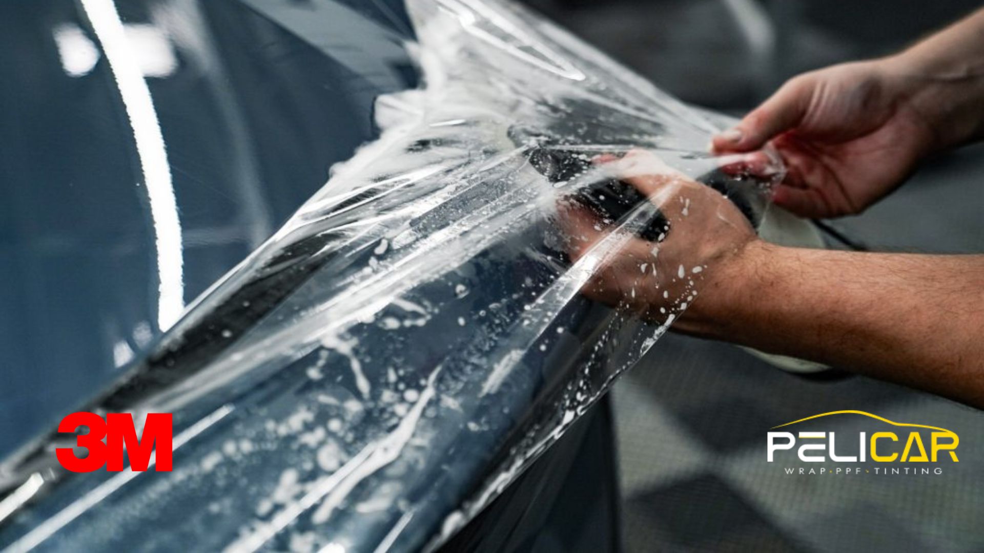 Paint protection film installation being carefully applied to a dark vehicle panel inside a professional auto shop.