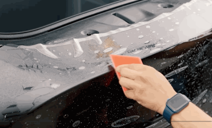 Technician smoothing paint protection film across a vehicle surface during professional PPF installation.
