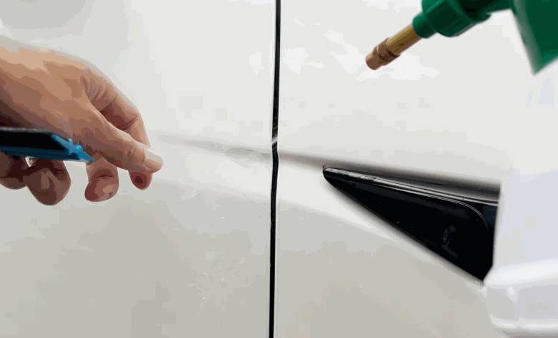Installer positions paint protection film along the panel edge of a white car near a black side trim piece.