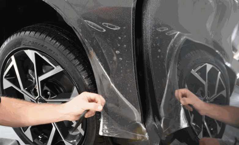 Installer pulls paint protection film into place on a gray car rocker panel near the rear wheel.