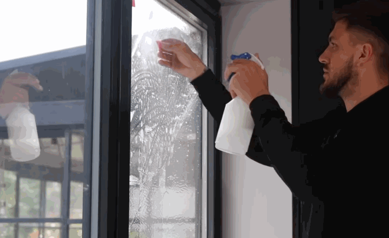 Installer sprays solution onto a residential style window while preparing the glass for window tint application.