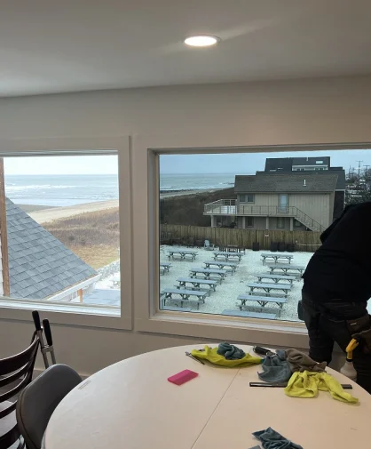 A person cleaning a window from the inside, with a beach view visible through the glass.