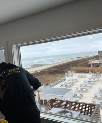 A person cleaning windows inside a room, with a view of the beach and a seating area below.